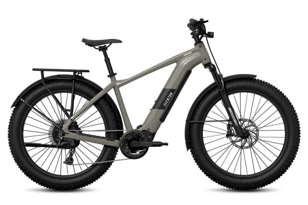 Side view of a grey-green Aventon Aventure M fat-tire electric bike showing its mid-mounted A100 motor, rear rack, black fenders and 4-inch knobby tires on a white background