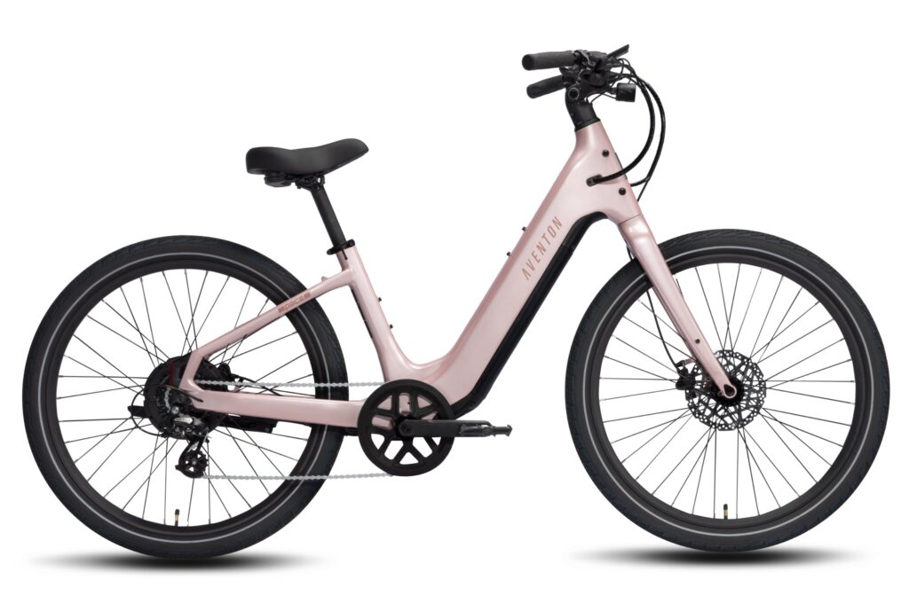 Side view of a pale pink Aventon Pace 5 REC step-through e-bike with a low frame, swept-back handlebars, 27.5-inch wheels and hydraulic disc brakes on a white background.